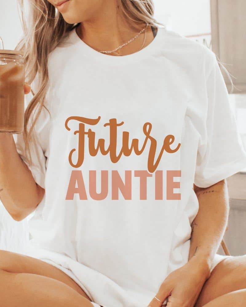 Woman wearing a white t-shirt that says Future Auntie in a tan and peach colored script.