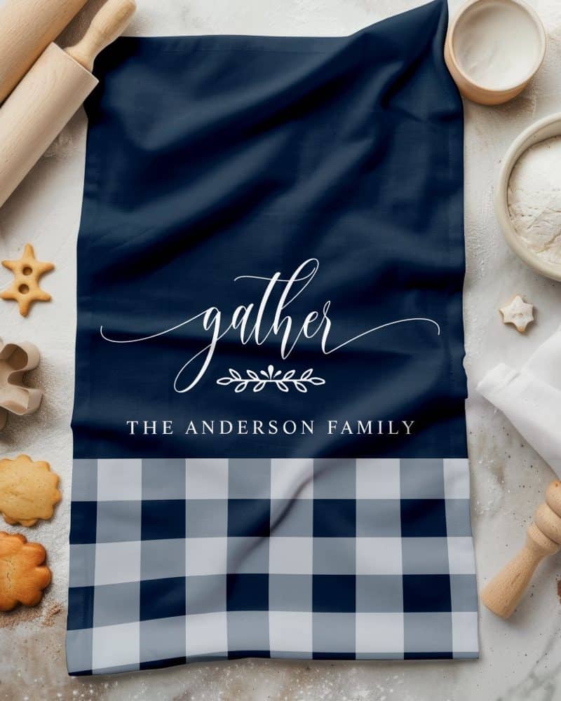 Navy blue and white checkered kitchen towel with the word gather and The Anderson Family printed on it.