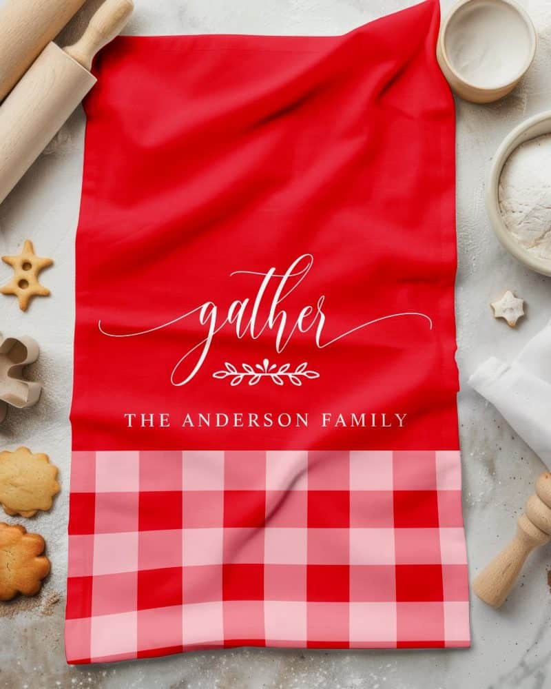 Red kitchen towel with the word gather in a script font and the Anderson family name. The bottom features a red and pink gingham pattern.