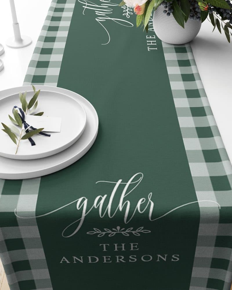 Green table runner with a light green and white gingham border, personalized with the word gather and the Andersons family name.