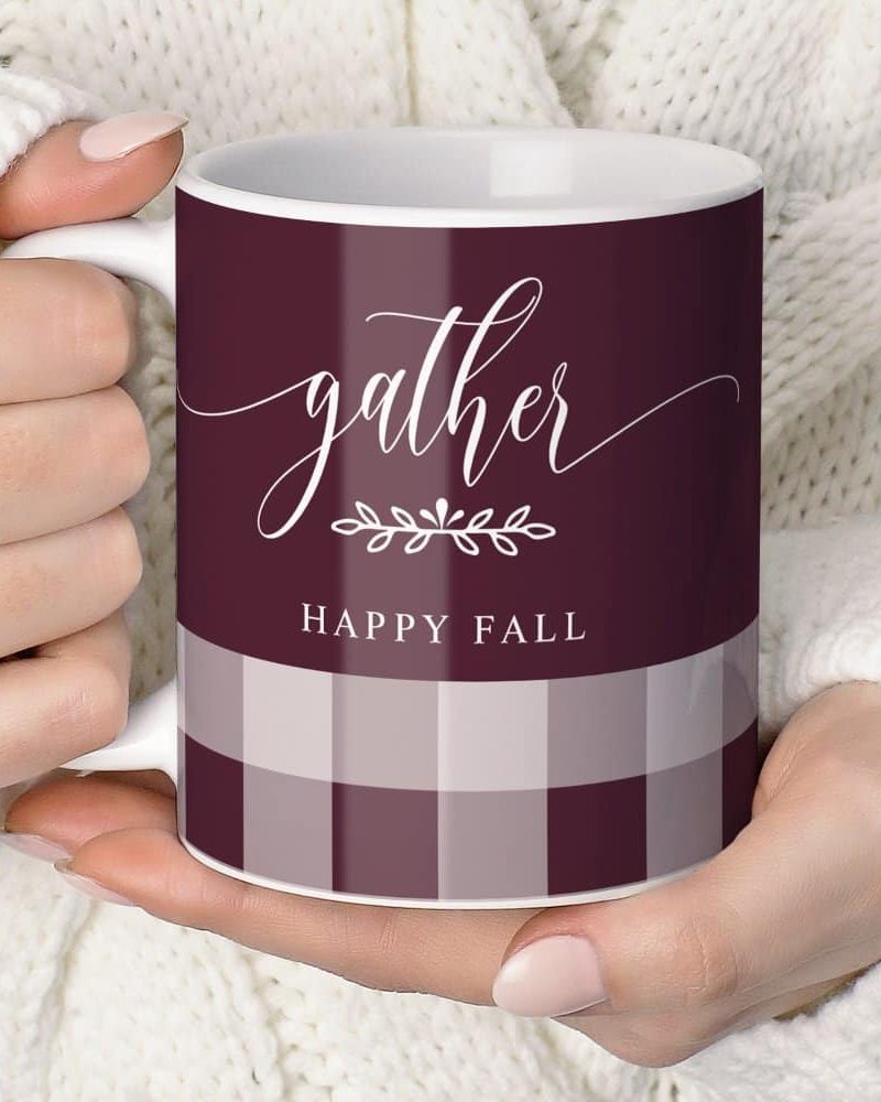 A person's hands holding a burgundy and cream plaid coffee mug that says Gather and Happy Fall.