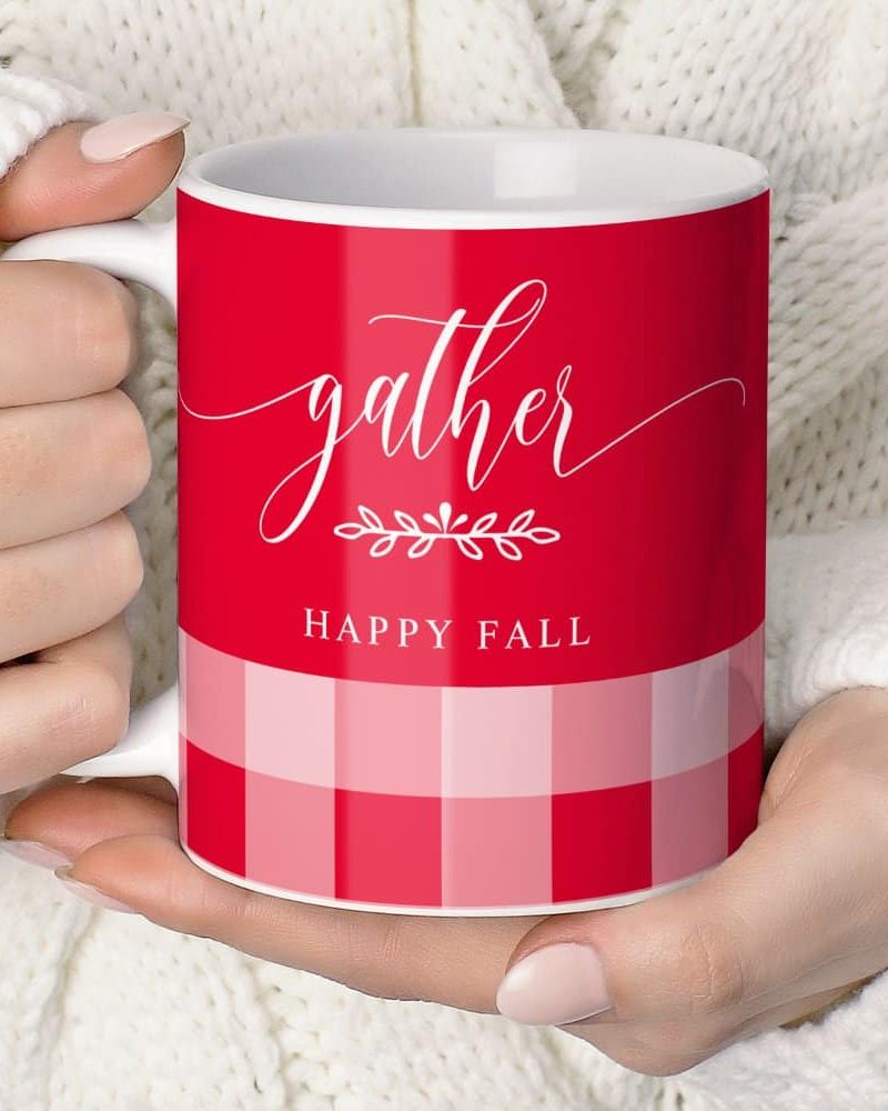 Two hands hold a red and pink checkered mug that says Gather and Happy Fall.
