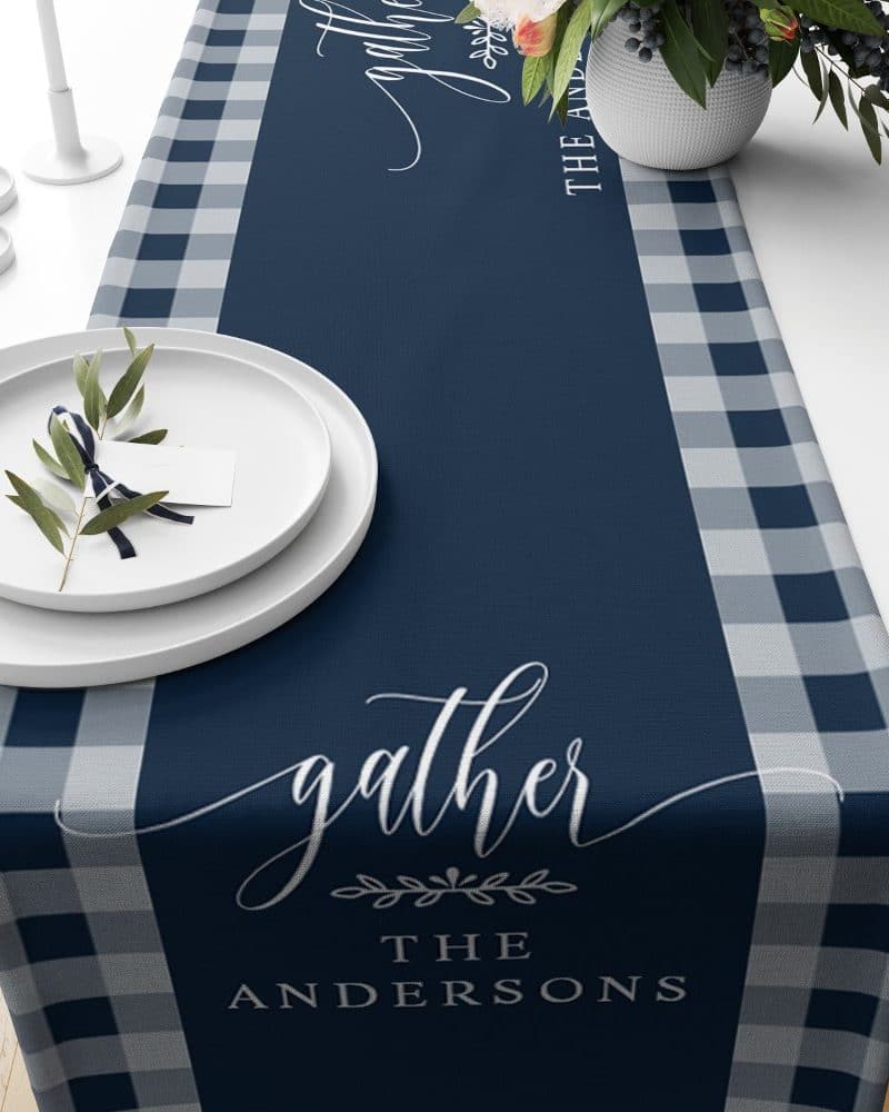 Navy blue table runner with gray and white gingham border, personalized with the word gather and the Andersons family name.