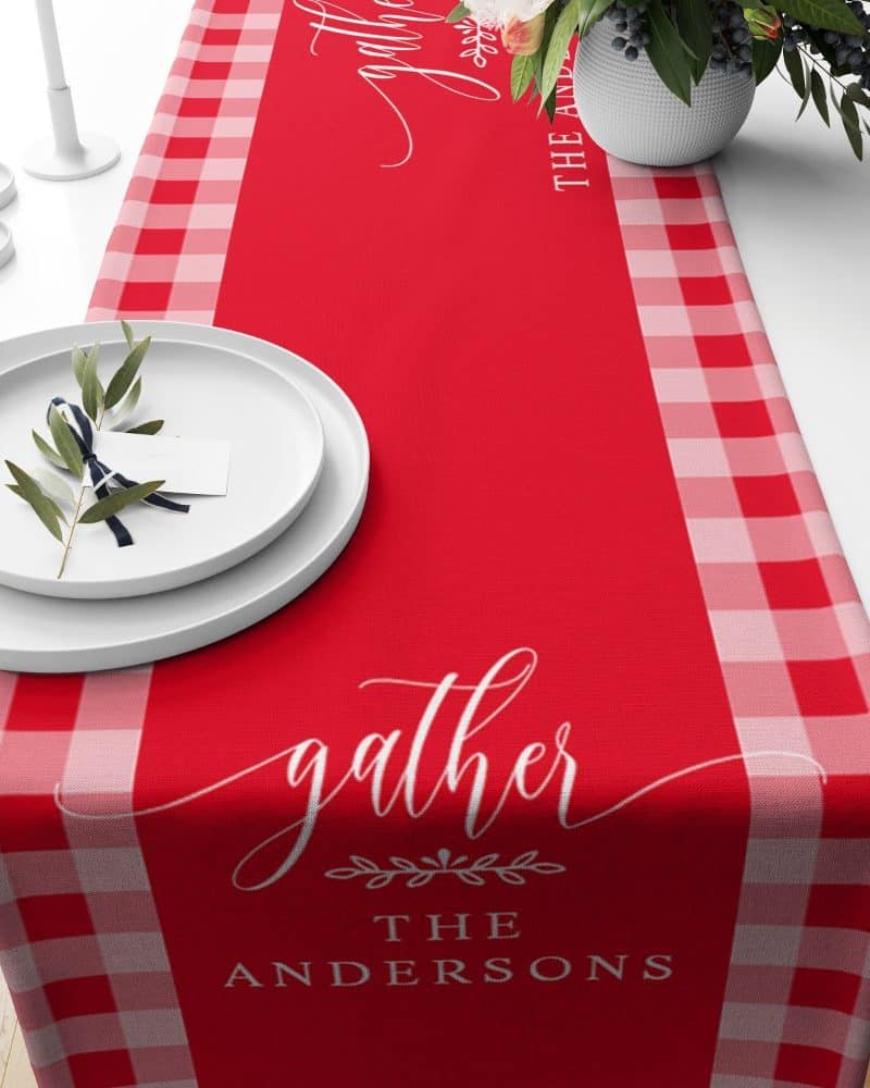 Red table runner with a pink gingham border and the word gather with The Andersons written below.