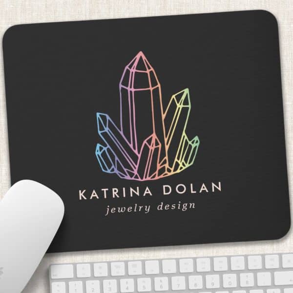 A Black Mousepad With A Pastel Rainbow Crystal Design And Katrina Dolan Jewelry Design Text.