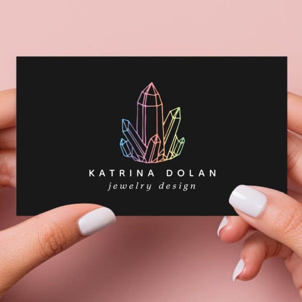 Two Hands Hold A Black Business Card Featuring A Pastel Rainbow Crystal Cluster Logo And The Text Katrina Dolan Jewelry Design.