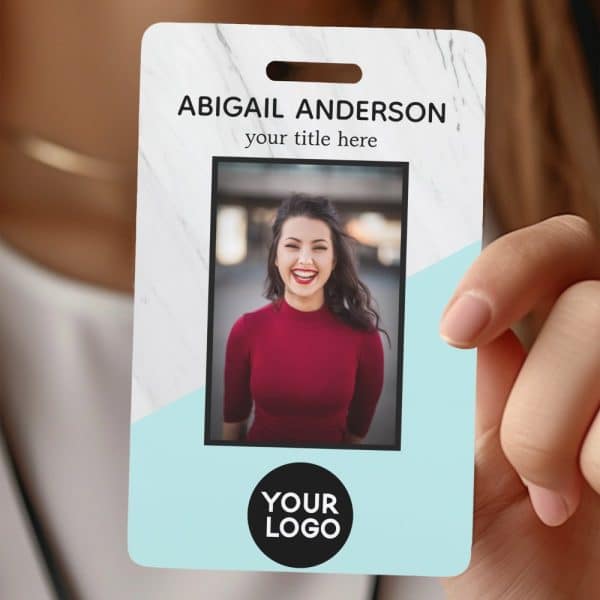 A Hand Holds A Marble And Light Blue Employee Id Badge With A Photo Of Abigail Anderson.