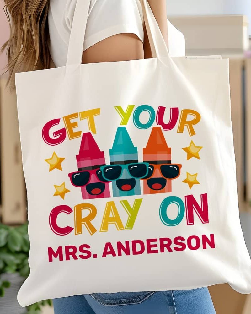 White tote bag with three cartoon crayons wearing sunglasses and the text Get Your Cray On, Mrs. Anderson.
