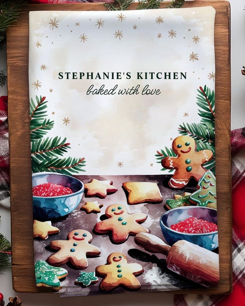 A kitchen tea towel featuring watercolor illustrations of gingerbread men and cookies, along with the text Stephanie's Kitchen baked with love.