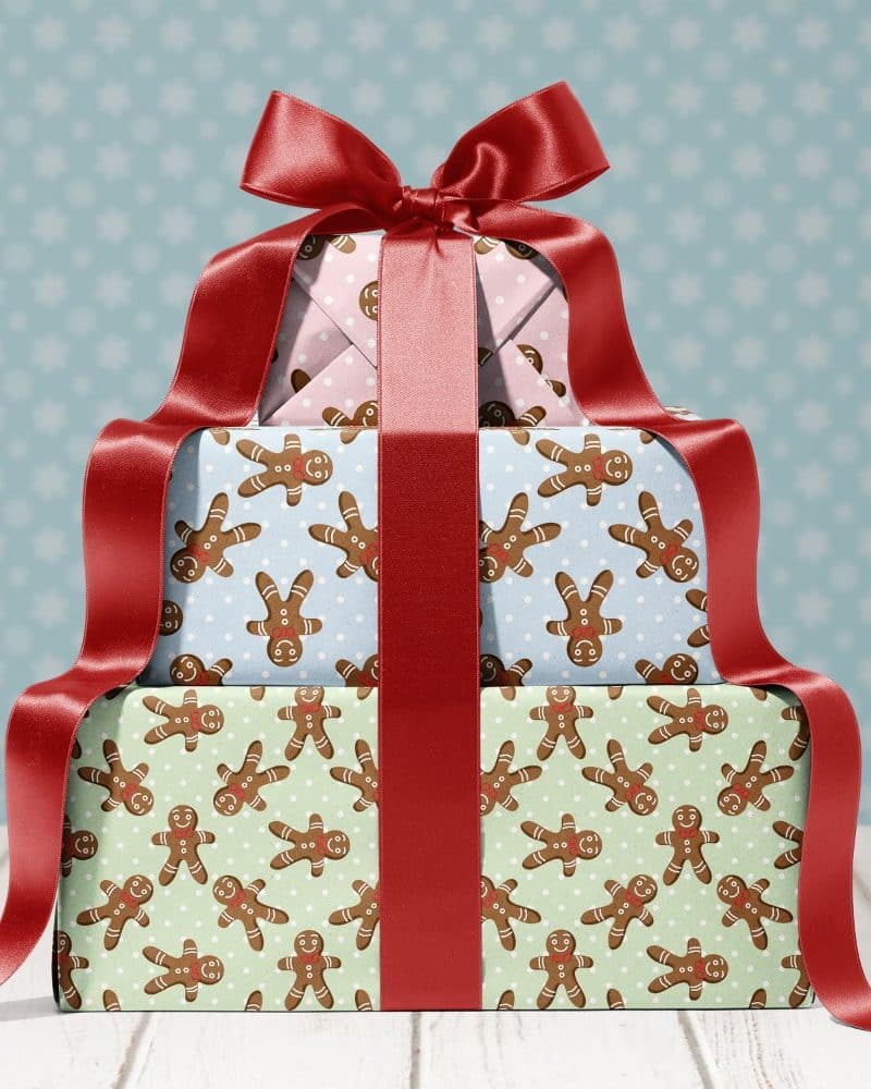 A stack of three Christmas presents tied with a large red bow. The presents are wrapped in paper featuring a gingerbread man pattern.