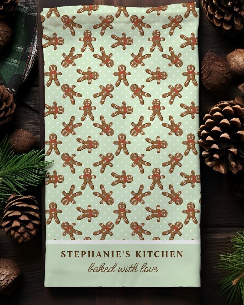 Kitchen towel with a repeating pattern of gingerbread men on a light green background. The bottom features personalized text.