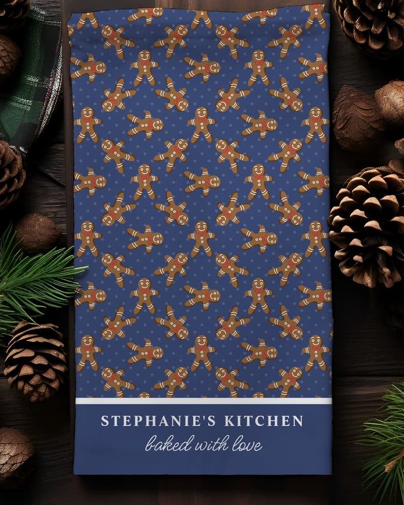 Blue kitchen towel with a repeating pattern of gingerbread men and the text Stephanie's Kitchen baked with love.