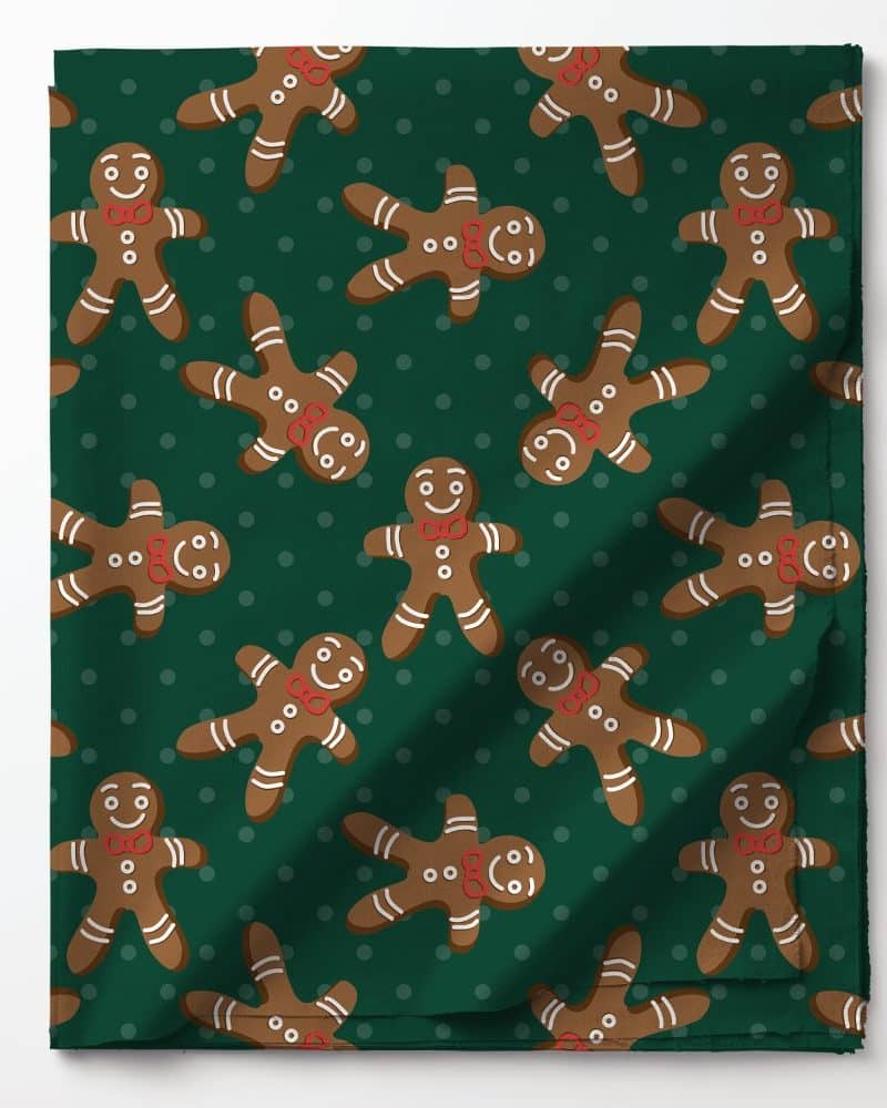 Green fabric with a repeating pattern of smiling gingerbread men wearing red bow ties.