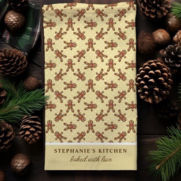 A Kitchen Tea Towel Featuring A Repeating Pattern Of Gingerbread Men On A Pale Yellow Background. The Bottom Of The Towel Is Personalized With Stephanie'S Kitchen Baked With Love.