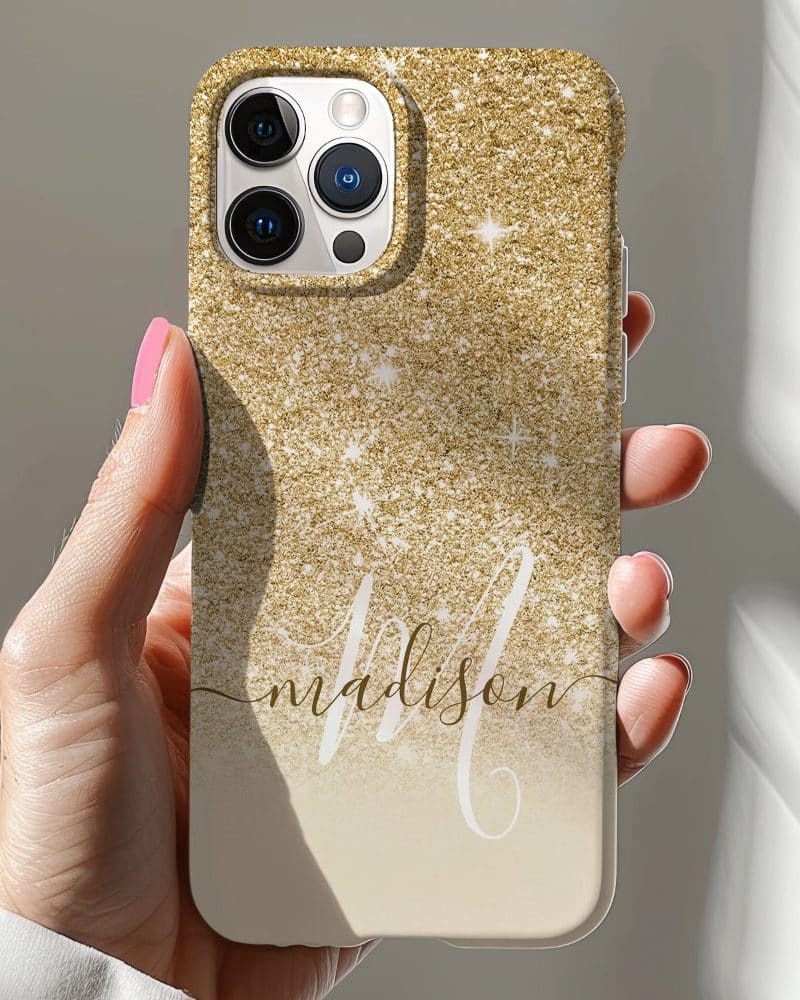 A hand holds a gold glitter iPhone case with the name Madison in elegant script.