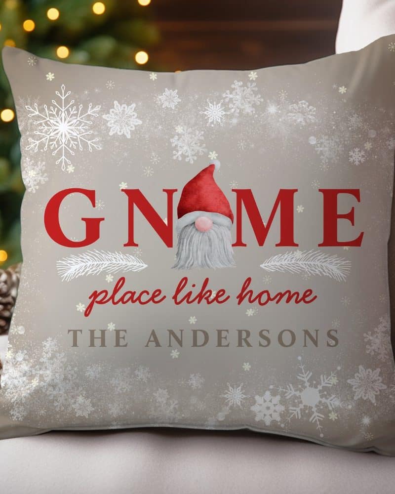 Tan Christmas pillow with a red-hatted gnome in the center of the word GNOME. The words place like home and the Andersons family name are also on the pillow, surrounded by snowflakes.