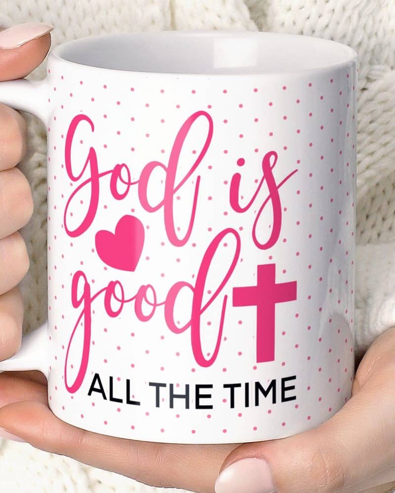 White coffee mug with pink lettering that reads God is good with a pink heart and cross, and All the Time at the bottom.
