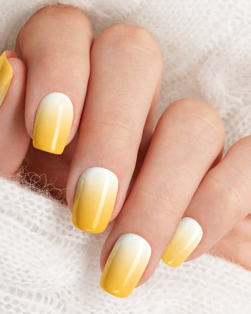 Close-up of a hand with yellow ombre nail polish.