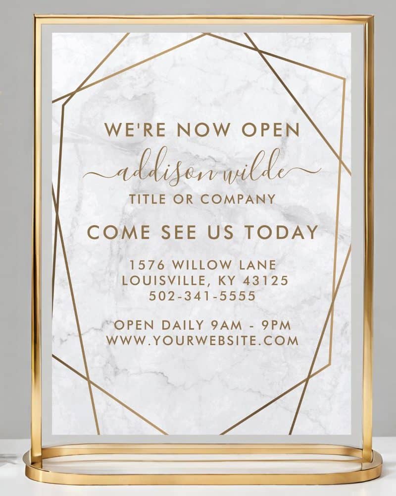 Gold-framed sign announcing Addison Wilde's grand opening, including address and hours.