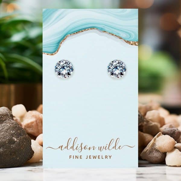 Pair Of Round Cubic Zirconia Stud Earrings Displayed On A Light Blue Jewelry Card.