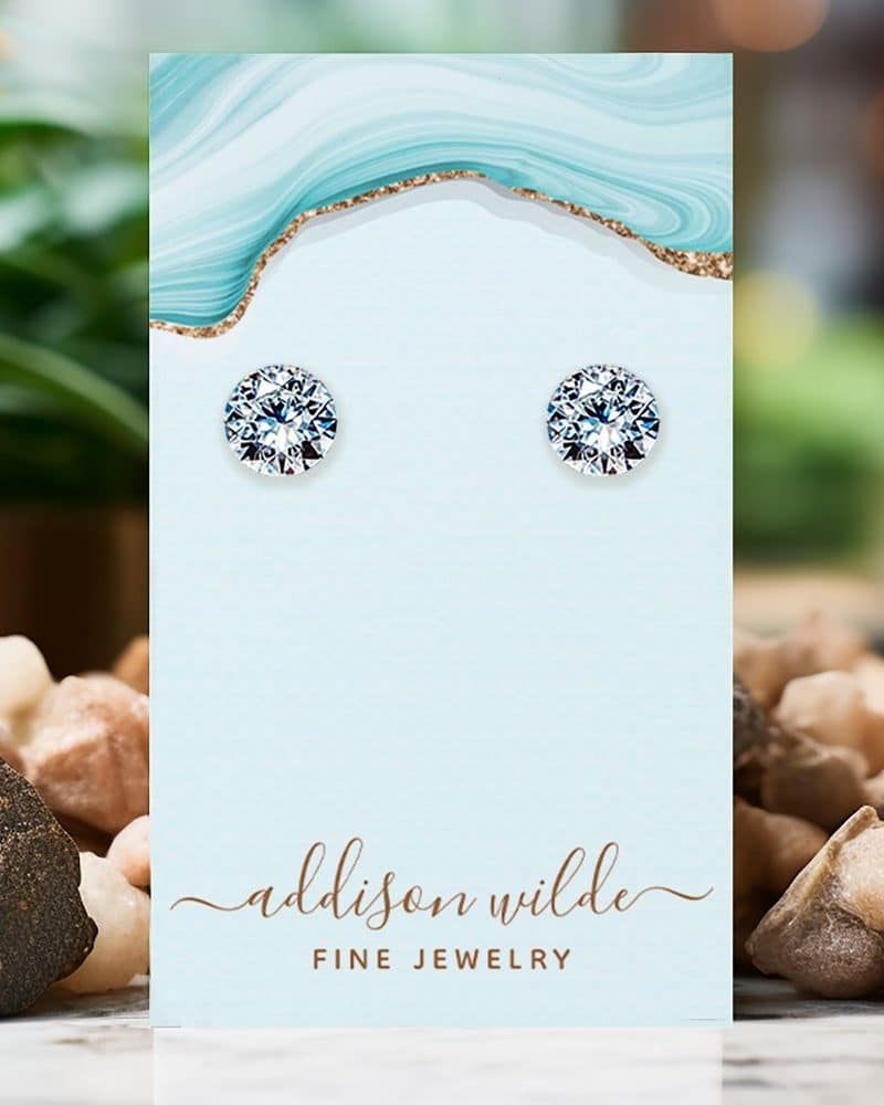 Pair of round cubic zirconia stud earrings displayed on a light blue jewelry card.