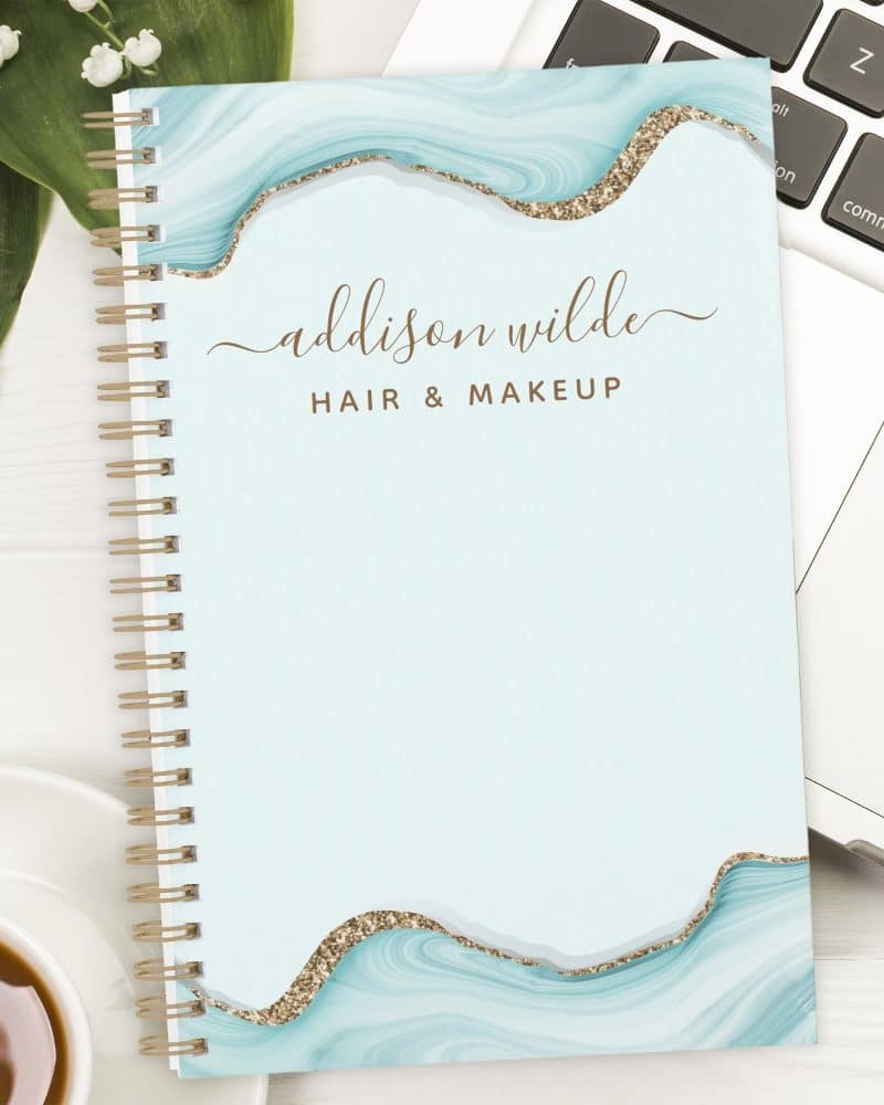 Spiral-bound notebook with a light blue marble design, gold glitter accents, and the name Addison Wilde Hair & Makeup.