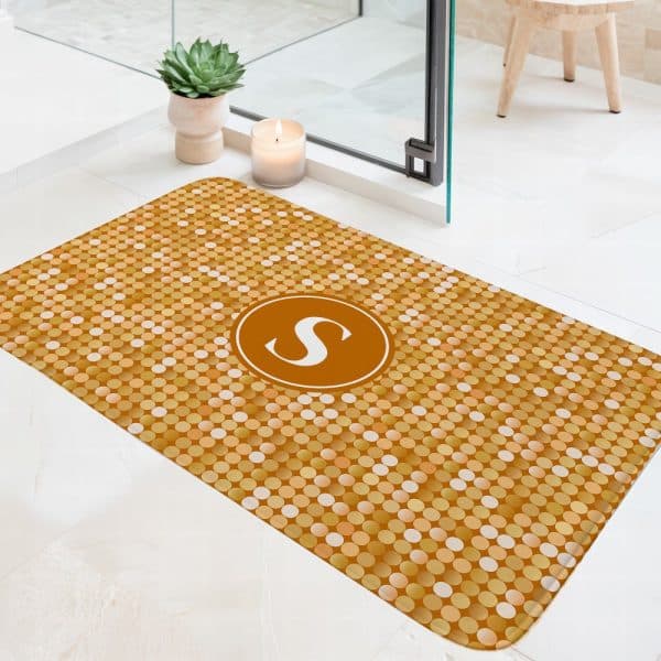 Gold Bath Mat With A Pattern Of Small Circles And The Letter S In A Circular Emblem In The Center.