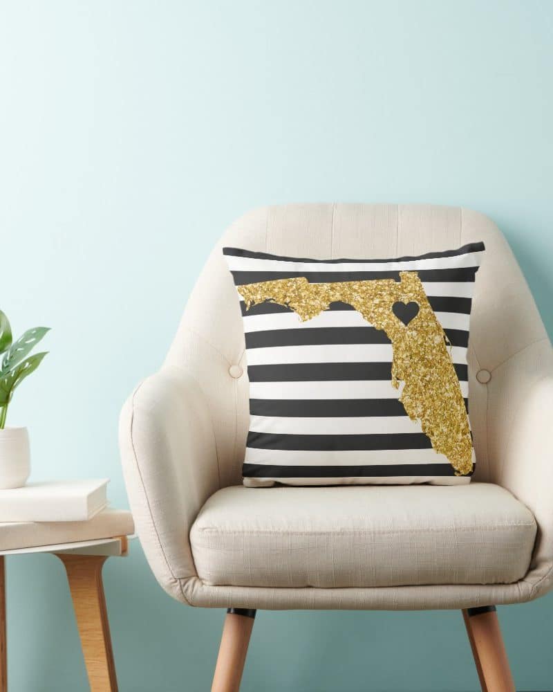 Gold glitter Florida shaped pillow on black and white striped fabric.