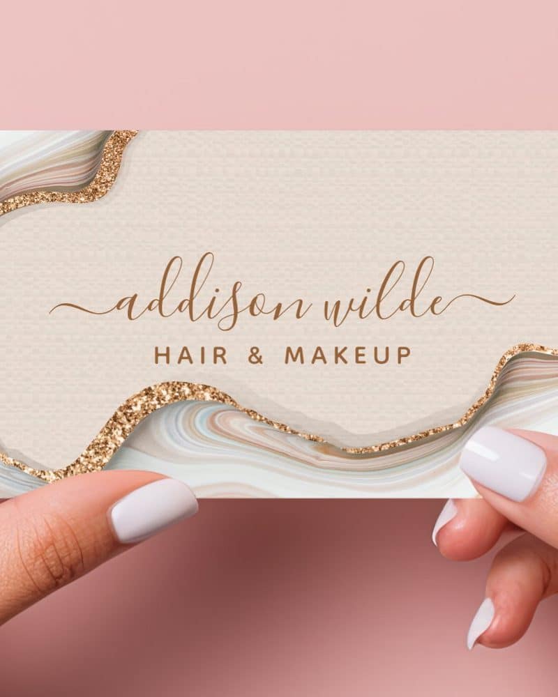 A business card for Addison Wilde Hair & Makeup. The card features a beige background with an agate design and gold glitter accents.