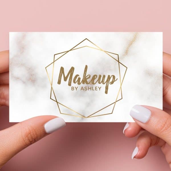 Two Hands Hold A Makeup Artist Business Card. The Card Features A Marble Design And Gold Geometric Frame With The Text Makeup By Ashley.