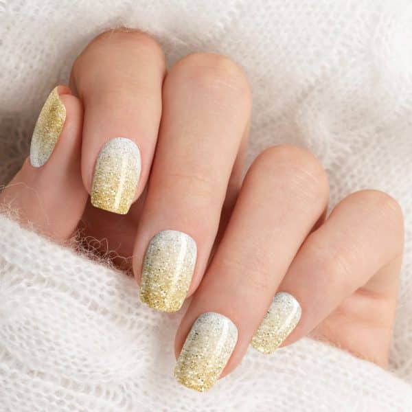 Close-Up Of A Hand With Fingernails Painted In A Gold And White Glitter Ombre Design.