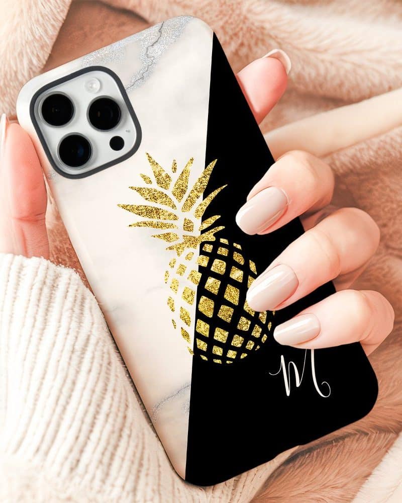 A hand holding a phone case featuring a gold glitter pineapple design on a marble and black background.