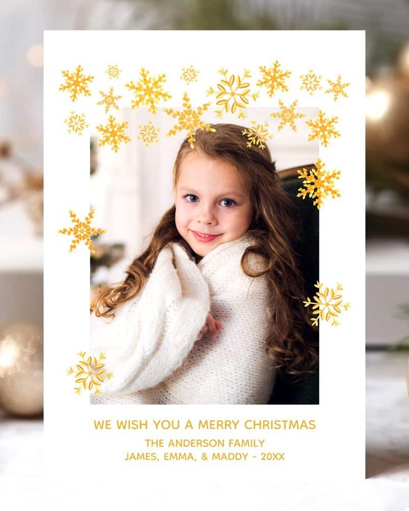 Christmas card featuring a young girl wrapped in a white blanket, surrounded by gold snowflakes.