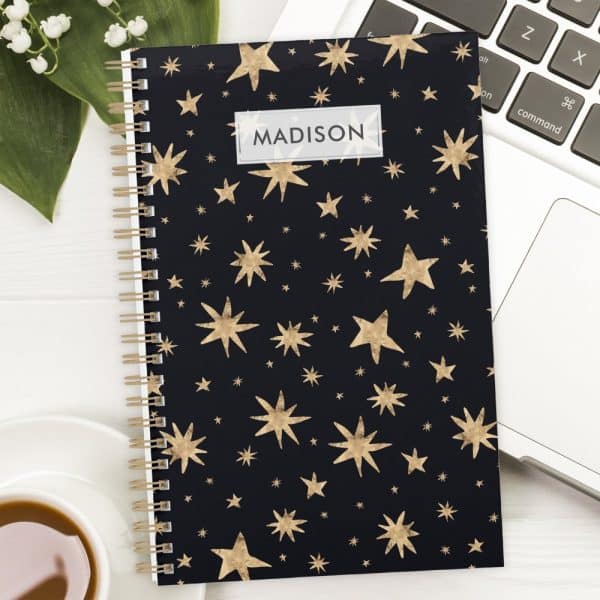 Spiral-Bound Notebook With A Dark Background And Gold Star Pattern; The Name Madison Is Printed On The Cover.