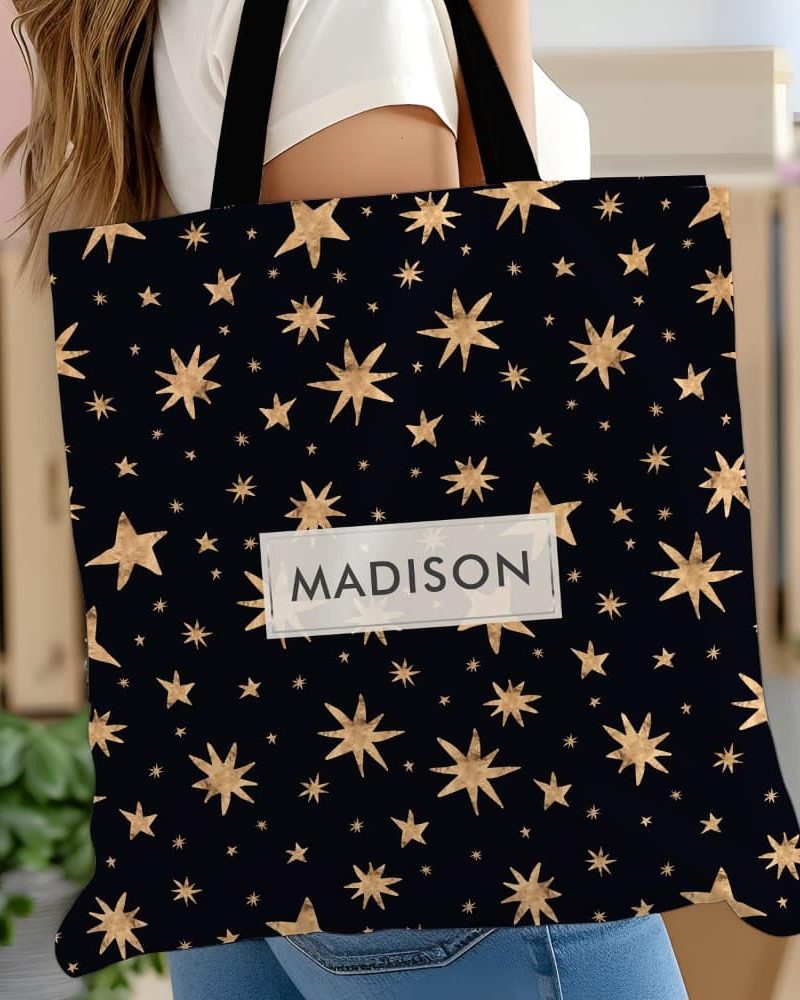 Personalized tote bag with gold stars on a black background. The name Madison is printed on the bag.