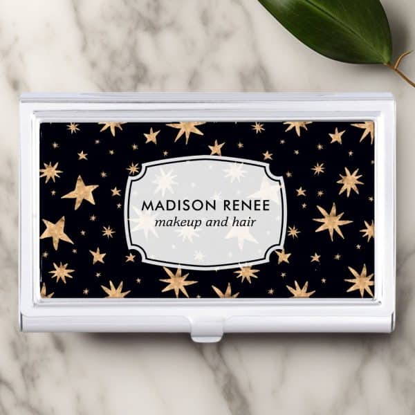 A Business Card Holder With A Black Background And Gold Stars; The Name Madison Renee Makeup And Hair Is In A White Label On The Holder.