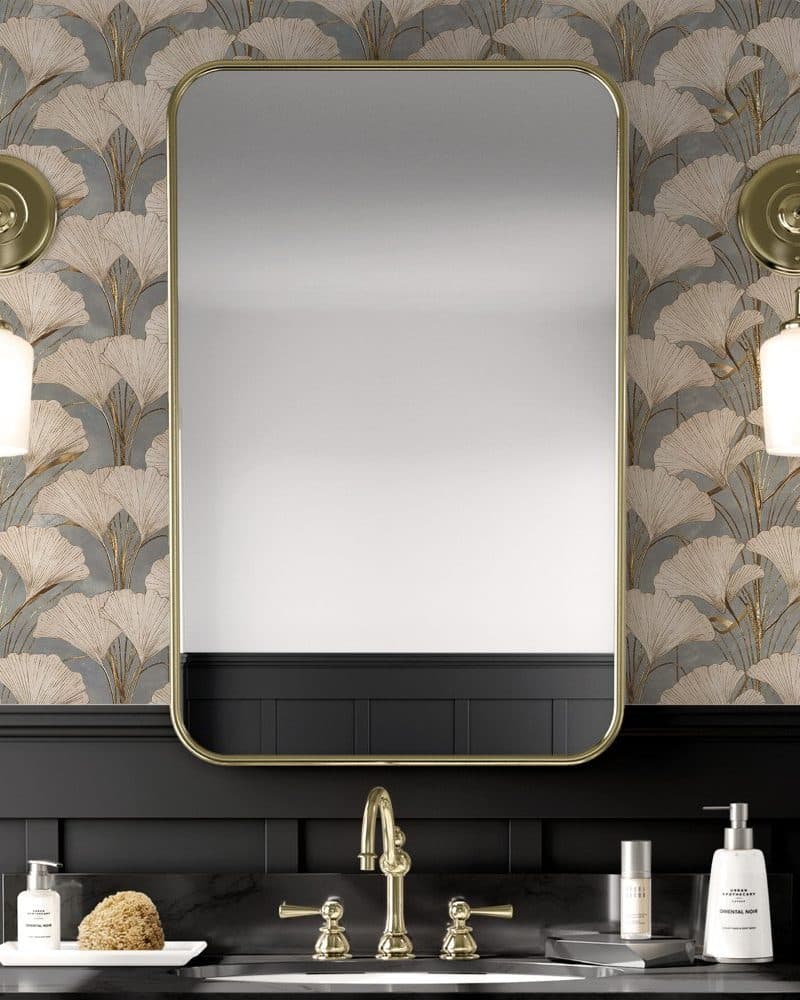 Brass framed mirror above a bathroom sink with gold leaf ginkgo biloba wallpaper.