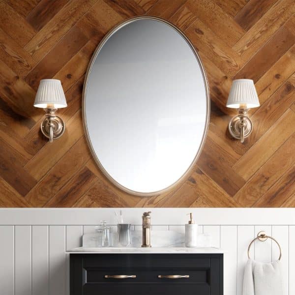 Oval Mirror Above A Bathroom Vanity With Dark Cabinets And Marble Countertop.