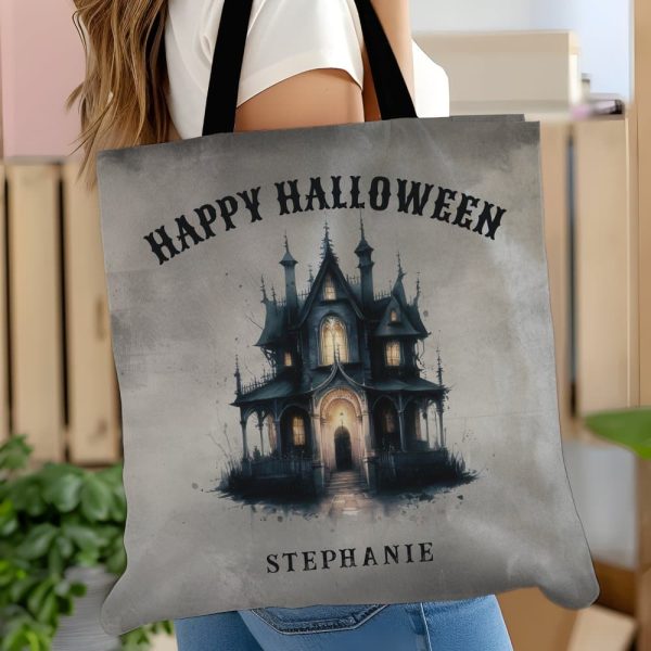 A Gray Tote Bag Featuring A Spooky Halloween Illustration Of A Large, Dark House With Lights In The Windows. The Text Happy Halloween Is At The Top, And The Name Stephanie Is At The Bottom.