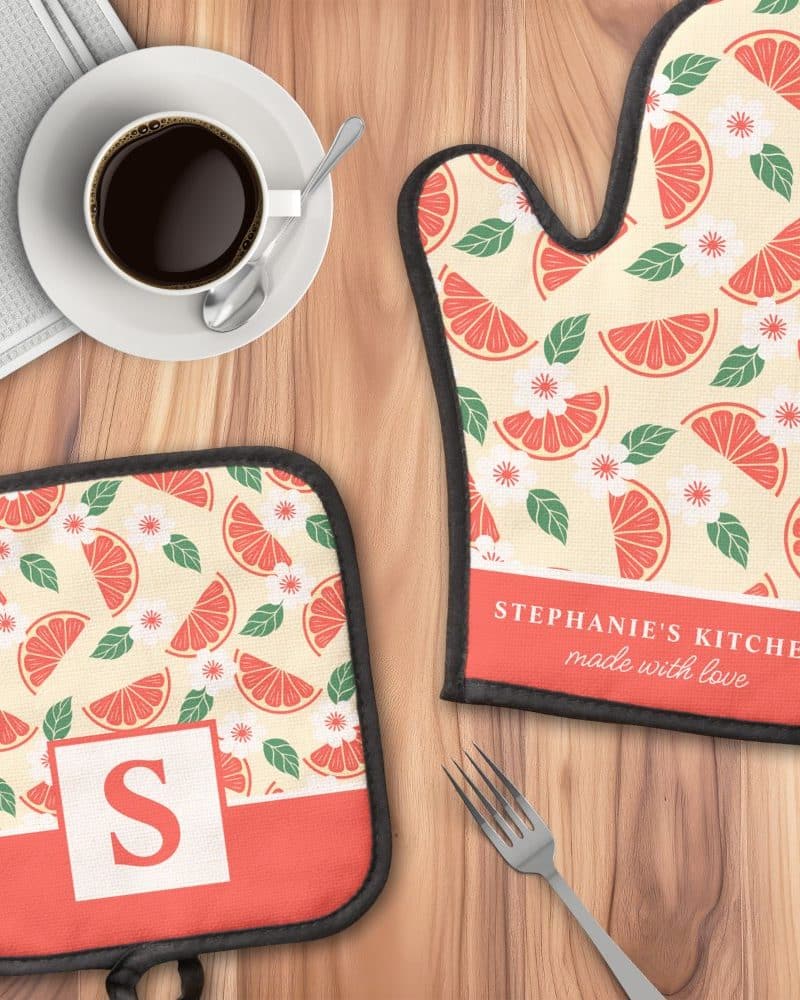 A personalized oven mitt and pot holder with a grapefruit and flower pattern. The oven mitt is labeled "Stephanie's Kitchen, made with love". The pot holder has a matching pattern and the initial "S".