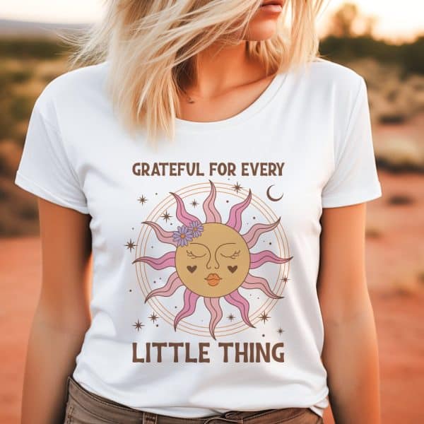 White T-Shirt Featuring A Sun Design With A Face And Flowers, And The Text Grateful For Every Little Thing.