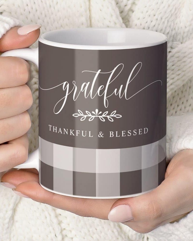A hand holds a coffee mug with a gray and white checkered pattern. The mug says grateful, thankful & blessed in a script font.