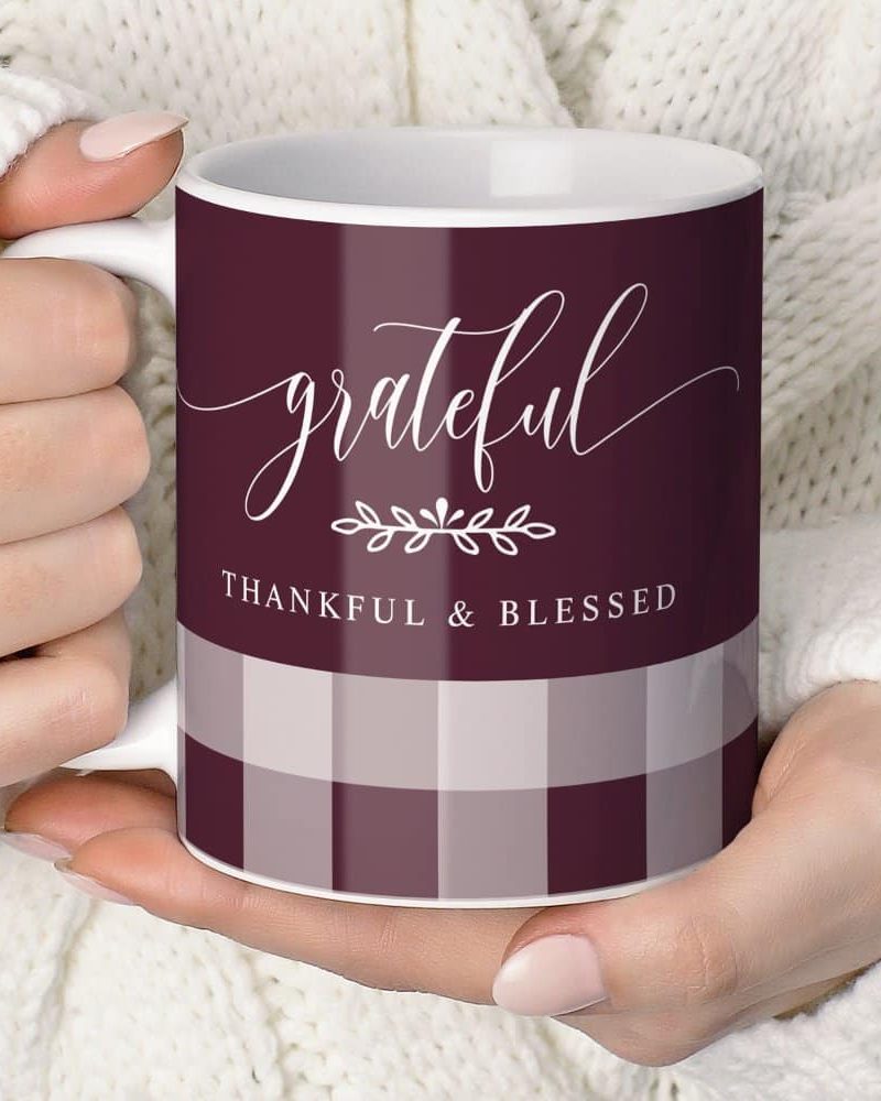 A person's hands holding a burgundy and cream plaid coffee mug that says grateful, thankful & blessed.
