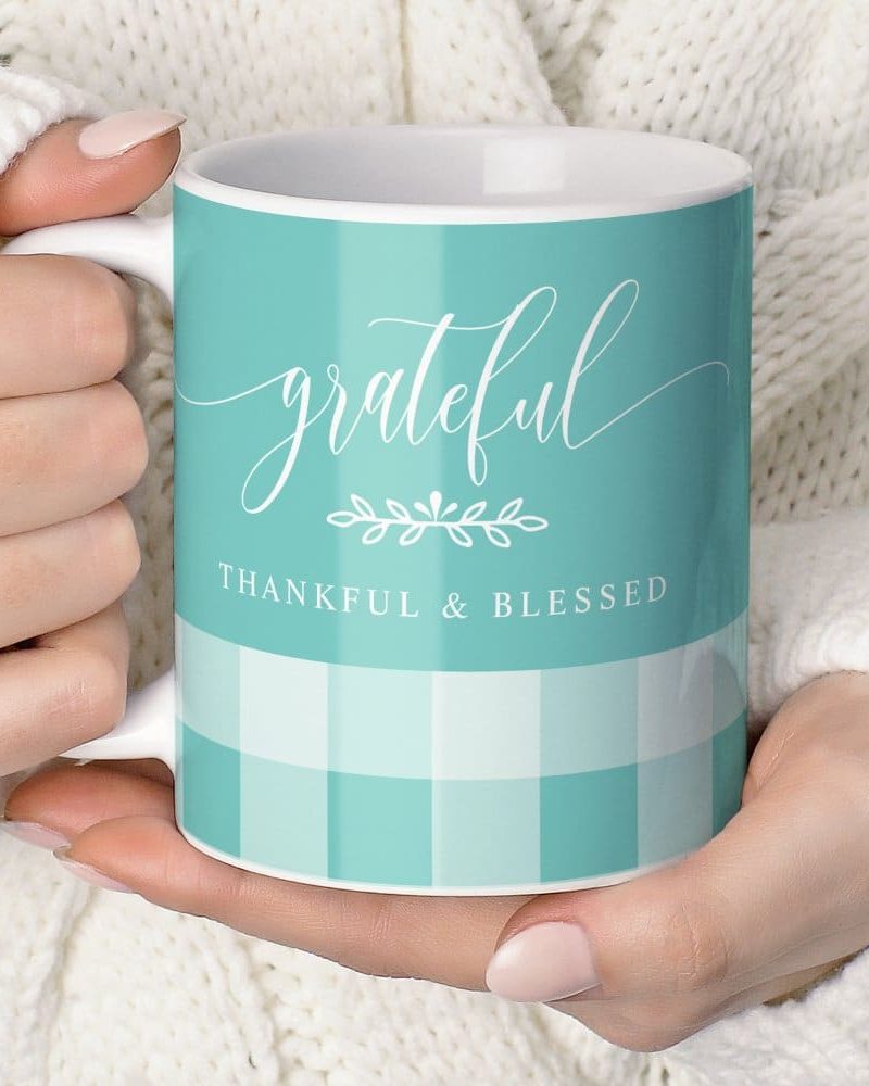 A teal coffee mug with the word grateful in elegant script, thankful & blessed below, and a subtle gingham pattern.