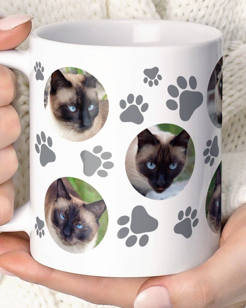 White coffee mug featuring multiple images of a Siamese cat and gray paw prints.