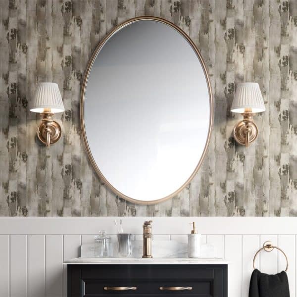 Oval Mirror With Brass Frame, Flanked By Matching Wall-Mounted Lamps, Above A Bathroom Vanity.
