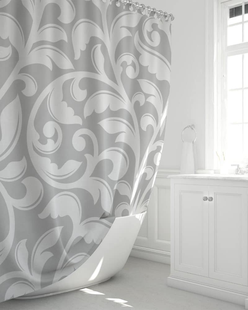 Gray shower curtain with a white damask pattern, partially draped over a white bathtub.
