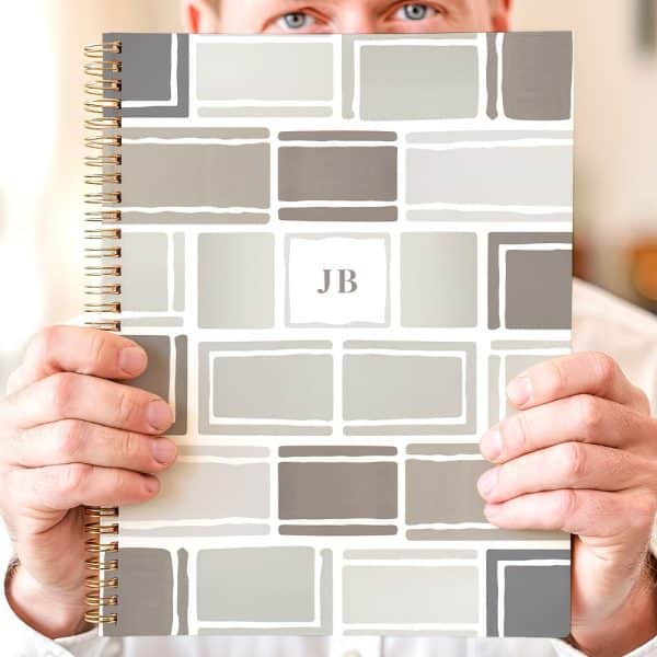 Person Holding A Spiral-Bound Notebook With A Geometric Design In Shades Of Gray And The Initials Jb.