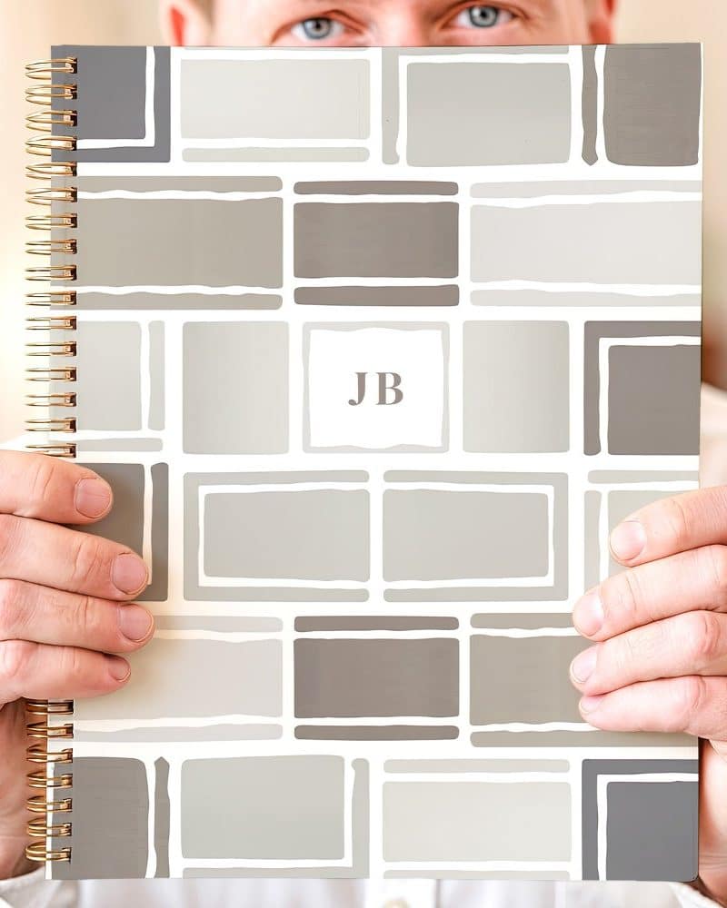 Person holding a spiral-bound notebook with a geometric design in shades of gray and the initials JB.