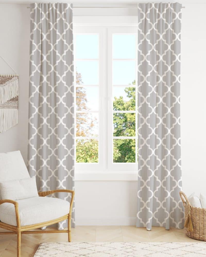 Grey curtains with a quatrefoil pattern hang in front of a window, next to a light grey armchair.